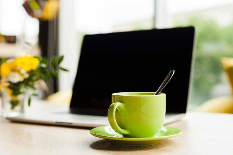 Eine Abbildung eines Schreibtisches mit einer grünen Kaffeetasse und einem Laptop.
