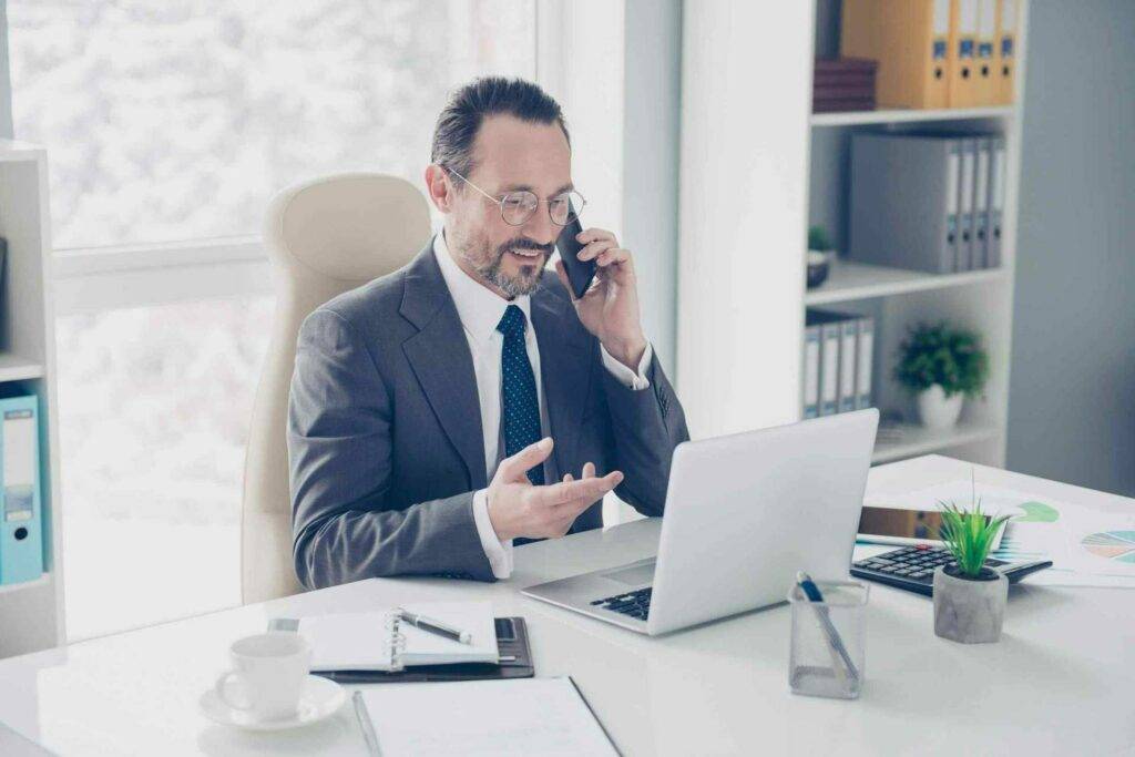 Ein Foto eines formell gekleideten Mitarbeiters, in einem hellen und modernen Büro, welcher konzentriert telefoniert.