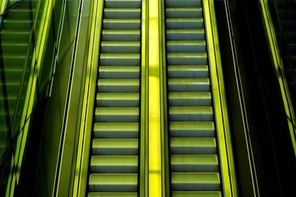 Eine Photographie einer grün beleuchteten Rolltreppe, welche ein Zeichen von Aufstieg und Effizienz darstellen soll.