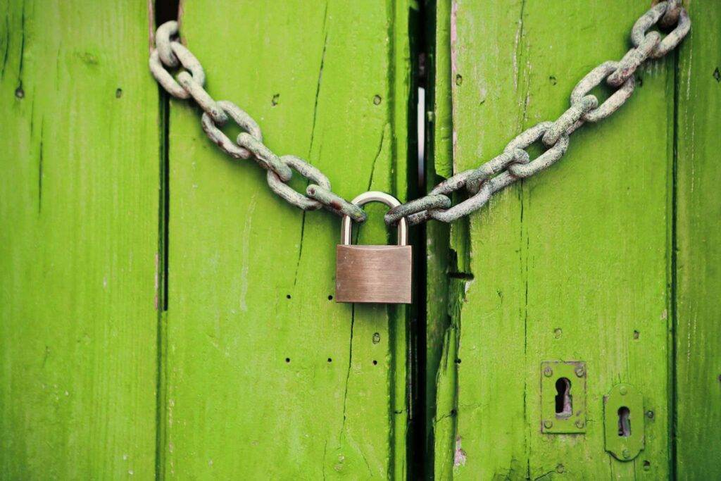 Ein Bild von einer Grünen Holztür, welche von einer Metallkette mit Schloss zugehalten wird. Die ist ein Symbol von Geheimnissen und Sicherheit.