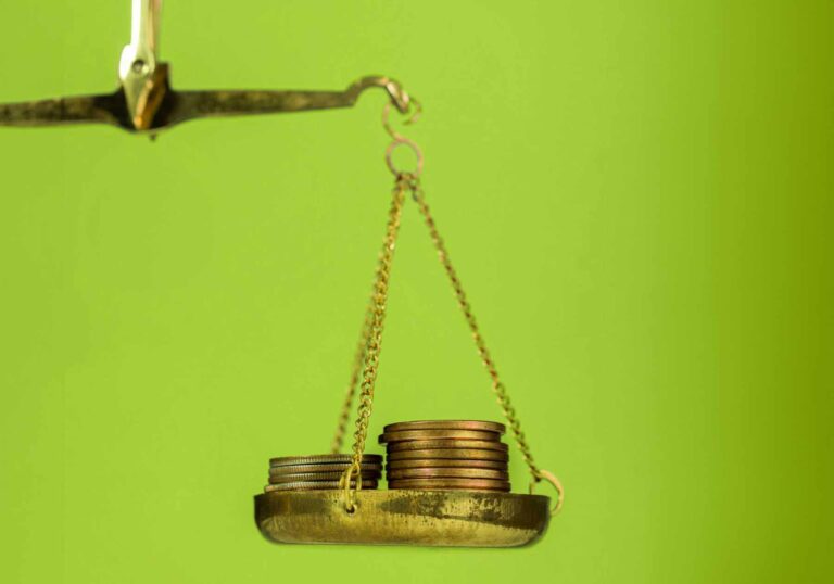 Ein Bild einer Wage mit einem Stapel Münzen vor grünem Hintergrund, als Symbol für Finanz - Management.