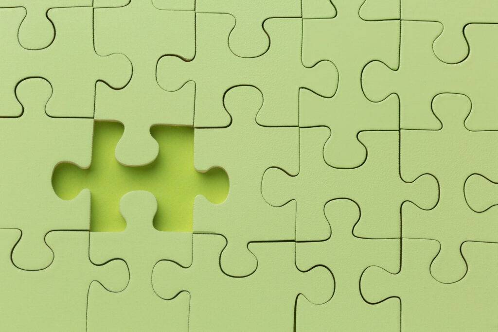 Ein Bild von einem einheitlich grünen Puzzle vor einem grünen Hintergrund. Ein Puzzleteil in der Mitte fehlt. Es symbolisiert das Ineinandergreifen von Abläufen und Vorgängen.