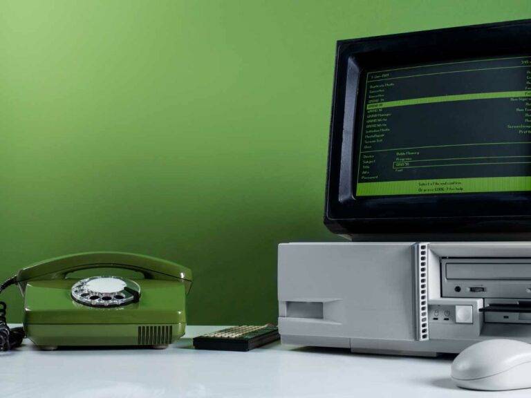 Vor einer grünen Wand ist ein Tisch auf welchem ein altes Telefon mit Wählscheibe steht und ein alter Computer. Es steht für die Erneuerung alter Technik und Upgrades der ERP-Systeme.