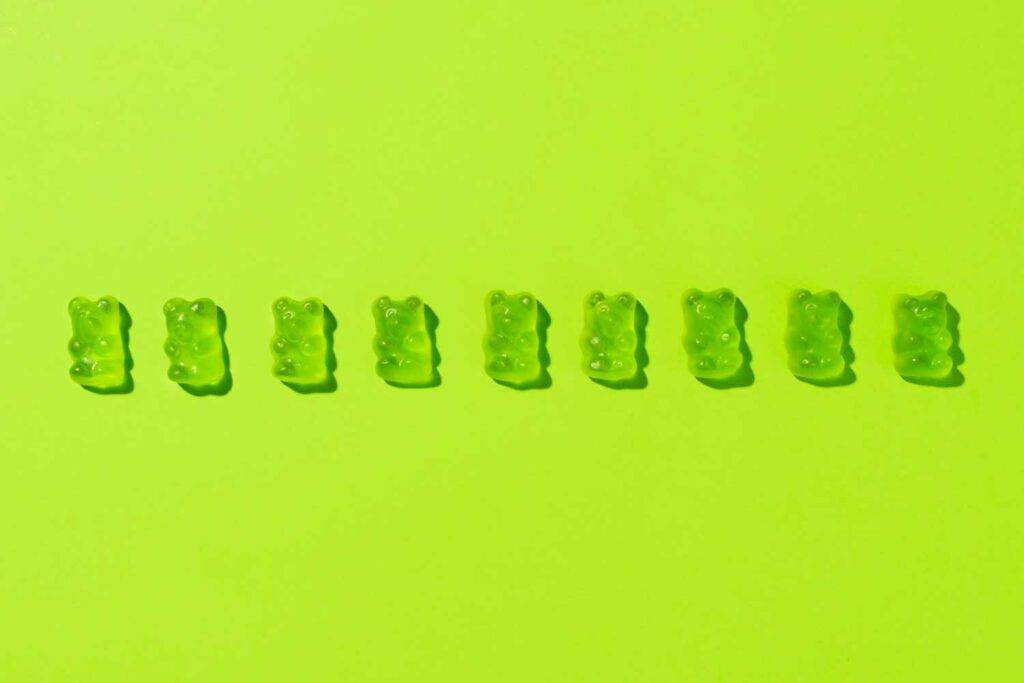 Auf dem Bild sieht man eine Reihe von grünen Gummibärchen vor einem grünen Hintergrund. Das Bild symbolisiert die Gestaltung.