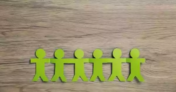 Symbolbild zu Rollen im Projekt. Fünf grüne Figuren aus Papier stehen Hand in Hand auf einer Holzoberfläche und symbolisieren Teamarbeit, Zusammenhalt und gemeinsame Projektverantwortung.