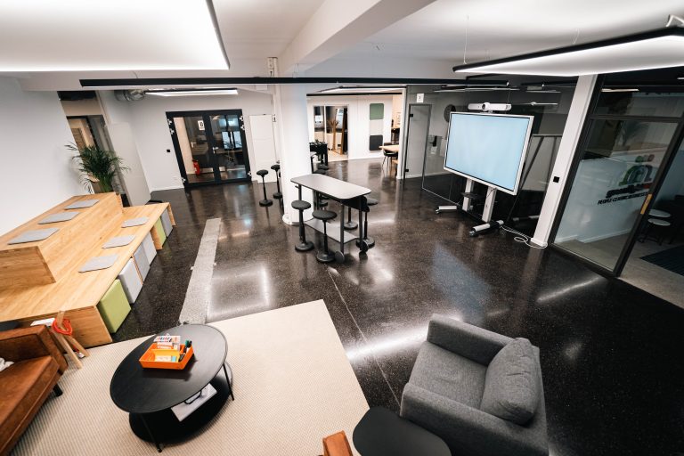 Moderner Meeting Raum, das GreenlightHUB mit moderner Medientechnik, flexiblem Raumkonzept, Steh- & Sitzarbeitsplätzen sowie großem professionellen Display inkl. Audio-& Videotechnik für professionelle Hybrid Meetings.