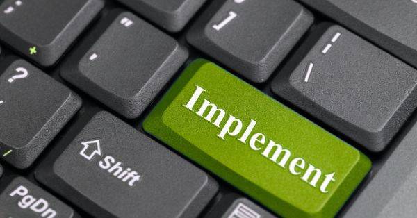 Tastatur mit hervorgehobener grüner „Implement“-Taste als Symbol für ERP-Implementierung mit Deltek Maconomy Powerlaunch