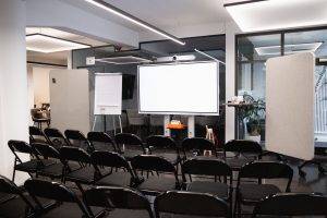 GreenlightHUB München mit Reihenbestuhlung vor großem Screen, Flipchart mit Ausrichtung Meetingraum.