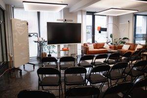 GreenlightHUB München mit Reihenbestuhlung Richtung Fensterfront/Street-View, großem Screen und Lounge-Bereich.