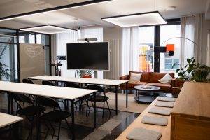 Workshopraum im GreenlightHUB München mit Reihenbestuhlung (3 Reihen), großem Screen, Flipchart und moderner Beleuchtung.
