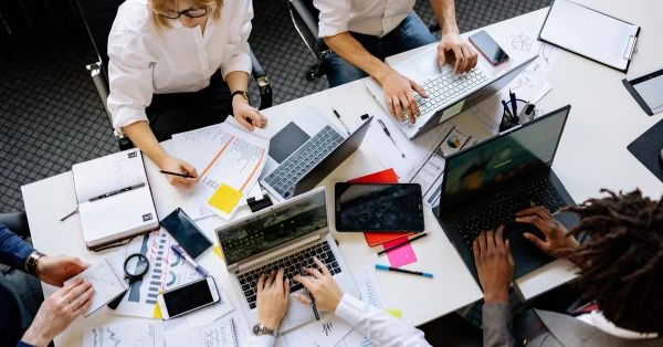 Team arbeitet gemeinsam an der Projektsteuerung mit Plänen, Laptops und Projektdaten auf einem Besprechungstisch.