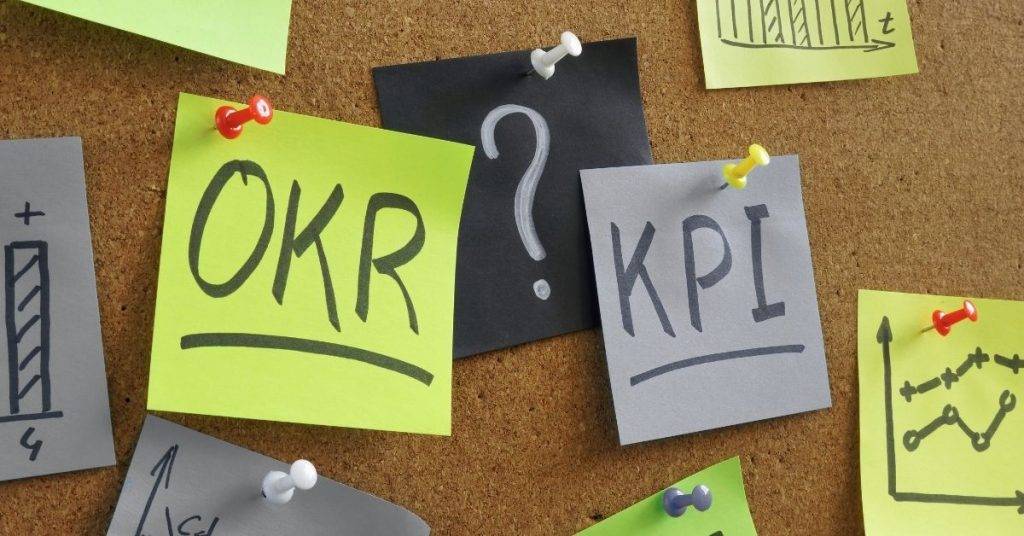 Pinnwand mit Notizzetteln zu OKR und KPI sowie Fragezeichen und Diagrammen als Symbol für Zielsetzung, Leistungsmessung und den Unterschied zwischen Objectives and Key Results und Kennzahlen.