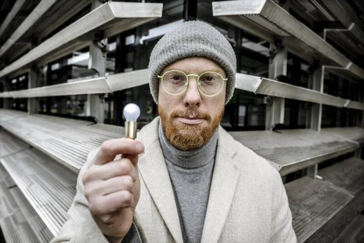 Porträt von Marcel Pesch, Keynote Speaker auf der Greenlight Connect 2026 zum Thema KI & Marketing. Er hat einen rötlichen Bart, zurückgebundene blondem Haar, dunkelblauem Anzug und weißem Hemd vor grauem Hintergrund.